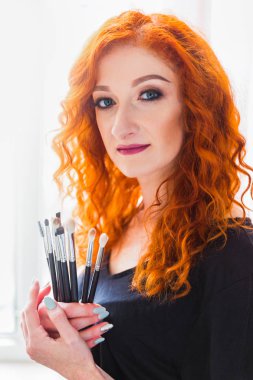 Makyaj fırçaları kapalı elinde tutan mutlu makyaj sanatçısı portresi