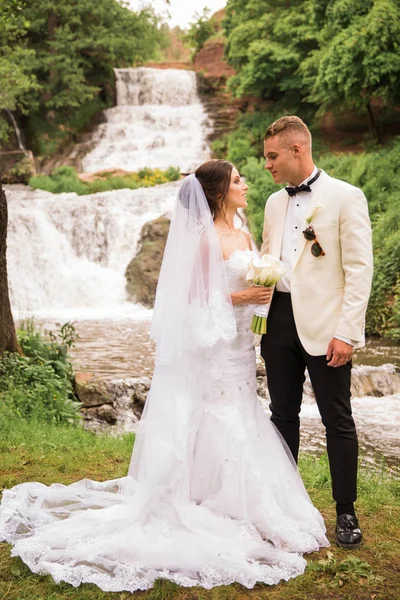 美丽的新婚夫妇在瀑布的背景下面对面站着 — 图库照片