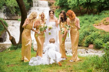 Neşeli gelin ve nedimeleri ve küçük bir çocuk bir şelale arka plan karşı duran ve gülümseyen