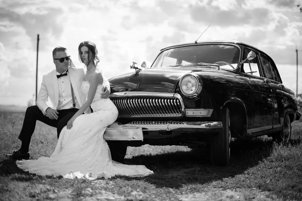 屋外の古い車のバンパーの上に座って幸せな新婚夫婦 — ストック写真