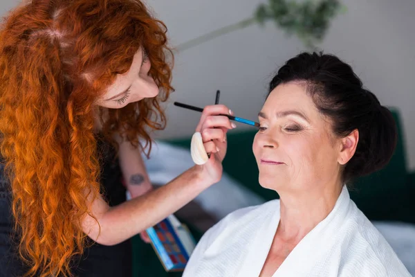 Makeup artist doing makeup to a happy woman indoor