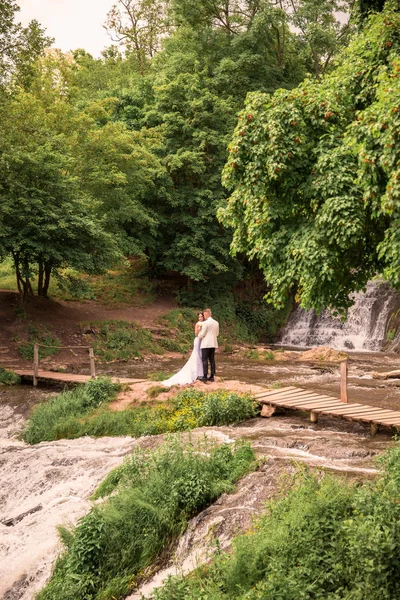 幸せな新婚夫婦滝の近くの石積みの抱擁で立っています — ストック写真