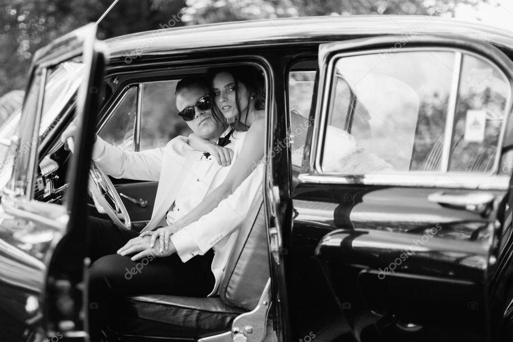 The happy beautiful newlyweds sitting in the embrace in the old car