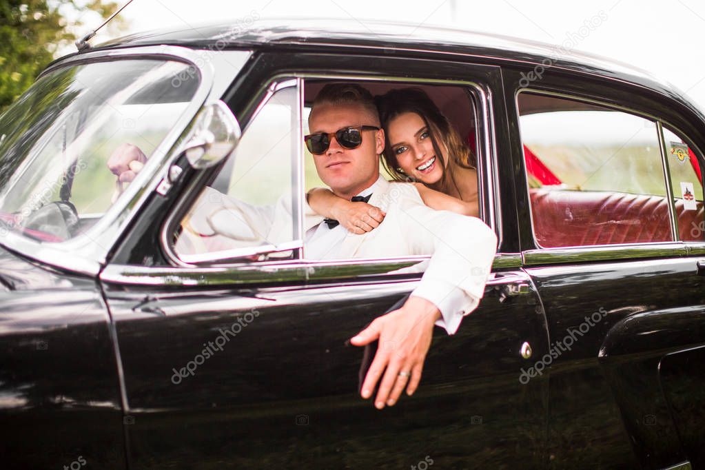 Happy, beautiful newlyweds sitting in the old car and smiling