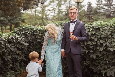 Zarif genç anne açık ayakta ve elinde şampanya kadehleri tutarak ve küçük oğlu onlara yakın duran ve annenin cam şampanya içme