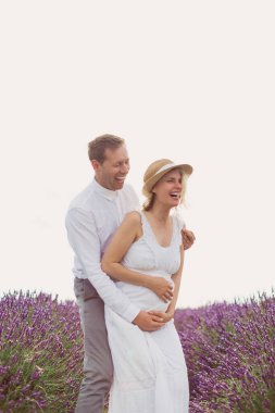 Gülümseyen genç adam, keyifli hamile karısıyla lavanta tarlasında kaliteli zaman geçiriyor.