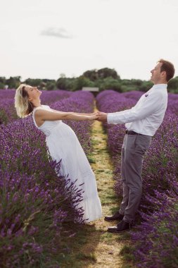 Genç adam lavanta tarlasında hamile karısının elini tutuyor.