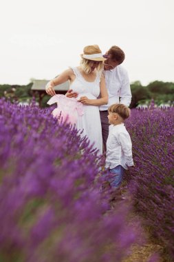 Sevimli bir çocuğu ve yeni doğmuş bebeği olan gülümseyen ebeveynler lavanta tarlasında duruyorlar.