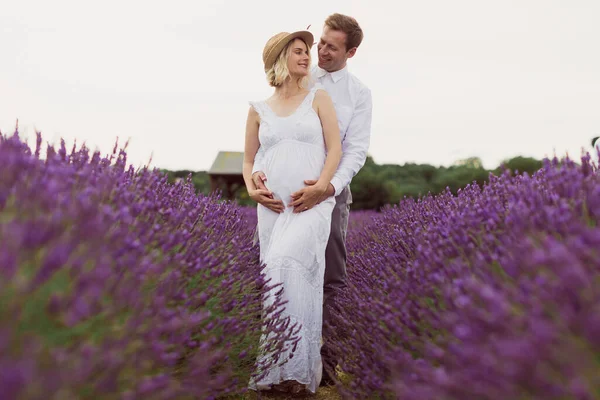 幸せな夫と妊娠中の妻はラベンダー畑の抱擁の中に立って笑っています — ストック写真