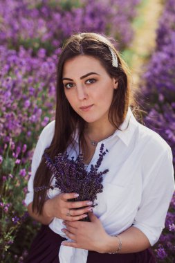 Lavanta tarlasında elinde çiçekleri tutan çekici bir esmerin portresi.