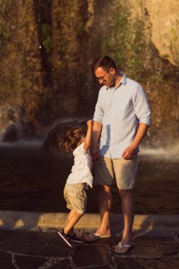 Genç baba, küçük oğluyla birlikte arka planda duruyor.