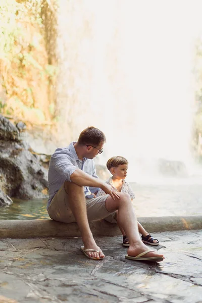 Jonge Vader Zit Met Zijn Zoontje Achtergrond Van Waterval — Stockfoto