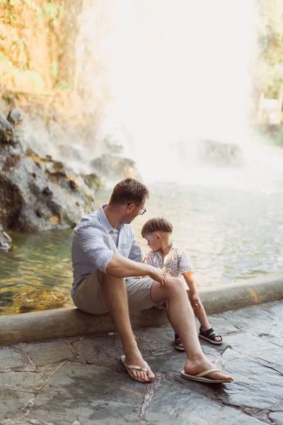 Gelukkige Jonge Vader Zit Met Zijn Zoontje Achtergrond Van Waterval — Stockfoto