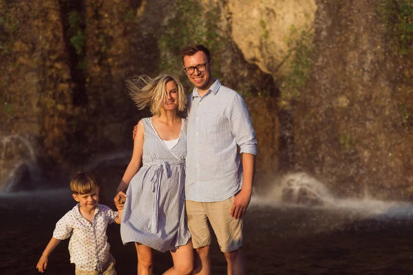 The smiling young pregnant family is standing on the rock background