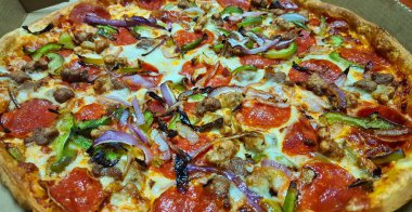 Yüce pizza kutusu kapağı açıkken, pişmiş kabuk dış kenarlarını gösterilen oturan Topingler ile.