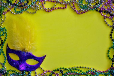 Renkli boncuk kolye köşedeki Venedik maskesi tarafından çerçeveli sarı bir Mardi Gras arka plan.
