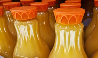 Ön planda odaklı bir süpermarket rafında portakal suyu şişeleri. Resmi kapat, kısmi kaplar ve kapaklar gösteriliyor.