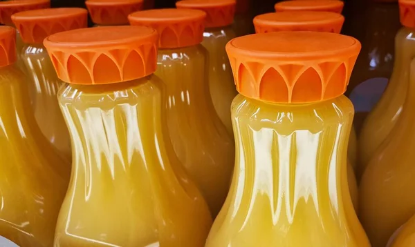 Orange juice bottles on a supermarket shelf with focus on foreground. Close up image, partial containers and lids shown.