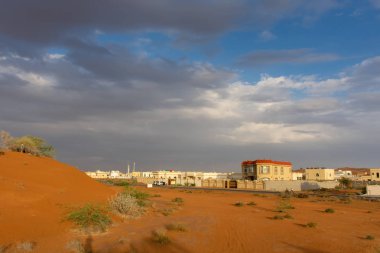 Ras al Khaimah, Birleşik Arap Emirlikleri karanlık, fırtınalı bulutlar ve şehir ve turuncu kum tepeleri üzerinde mavi gökyüzü ile fırtınalı bir akşam.