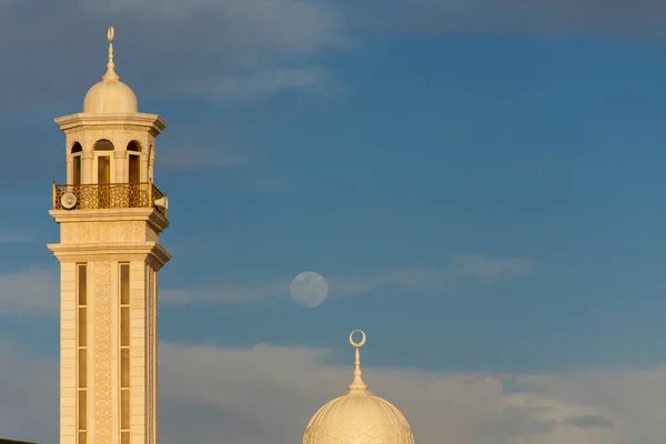 Une rare pleine lune de jour avec un ciel bleu derrière les minarets d'une mosquée locale aux Émirats arabes unis . — Photo