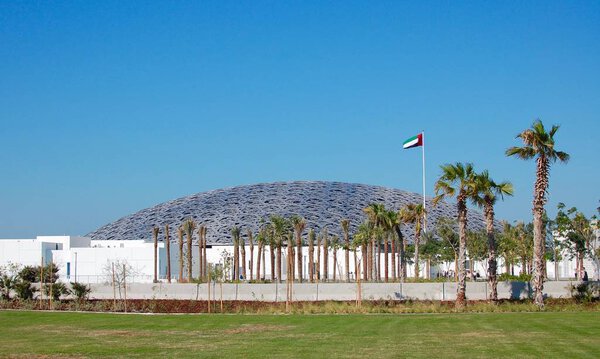 The Abu Dhabi Louvre is an impressive museum inside and out. Beautiful blue sky exterior with grass and flag