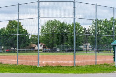 Baseball or softball diamond through a fence in park in a small clipart