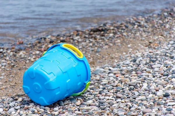 Blue bucket or pail on the seashore sitting empty in the rocky sand