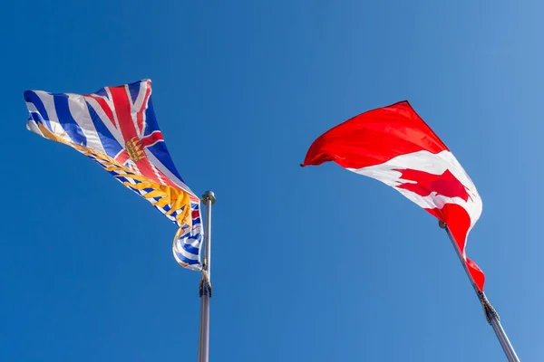 Mirando hacia arriba en la bandera de Canadá y Columbia Británica (BC) que sopla en el viento en un día soleado brillante . —  Fotos de Stock