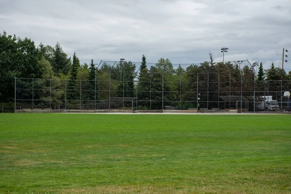 Empty baseball or softball diamond from the back fence and foul line looking towards the grass and trees in New Westminster, British Columbia, Canada.