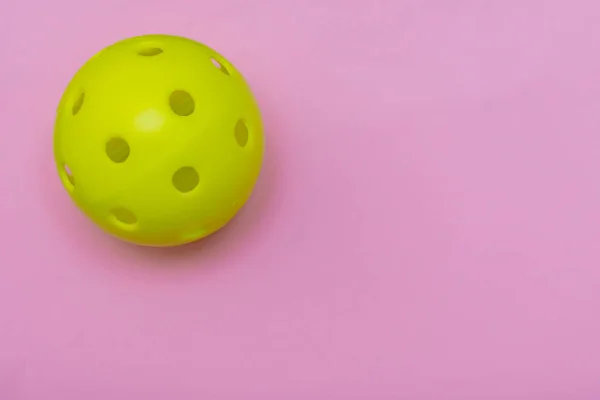 コピースペースでスポーツや活動を象徴する固体明るいピンクのフラットレイアウトの背景に明るい黄色のピックルボールや鞭ボール. — ストック写真