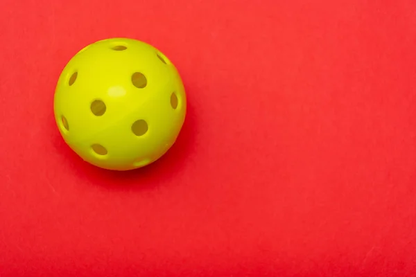 明るい黄色のピックルボールまたはコピースペースでスポーツやアクティビティを象徴するしっかりと明るい赤のフラットレイアウトの背景にあるホワイトボール. — ストック写真