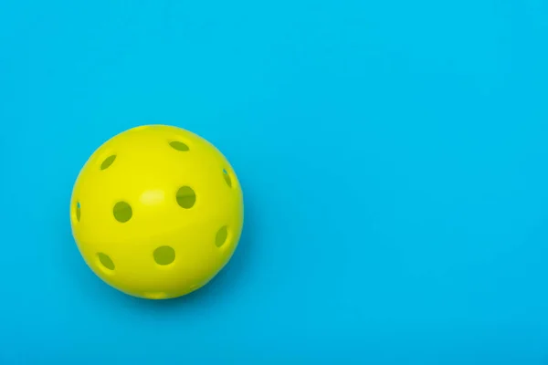 コピースペースでスポーツやアクティビティを象徴するソリッドアクアブルーのフラットレイアウトの背景に明るい黄色のピックルボールまたはホイップボール. — ストック写真