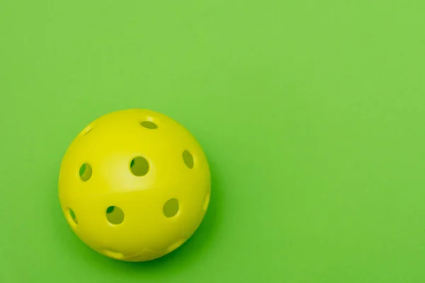 Açık yeşil düz zemin üzerinde parlak sarı bir picleball ya da Whiffle topu uzanmış fotokopi alanı ile spor ve aktiviteyi sembolize ediyor. — Stok fotoğraf