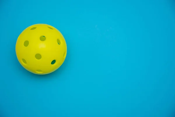 コピースペースでスポーツや活動を象徴する固体明るい青のフラットレイアウトの背景に明るい黄色のピックルボールや鞭ボール. — ストック写真