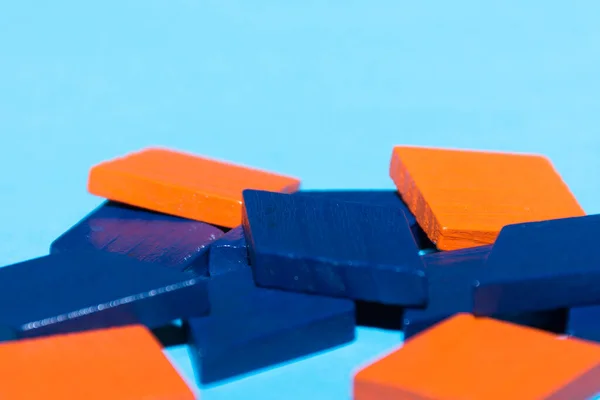 Bright colored blue and orange tangram child geometric shape puzzle pieces  in a pile close up on blue background with copy space.