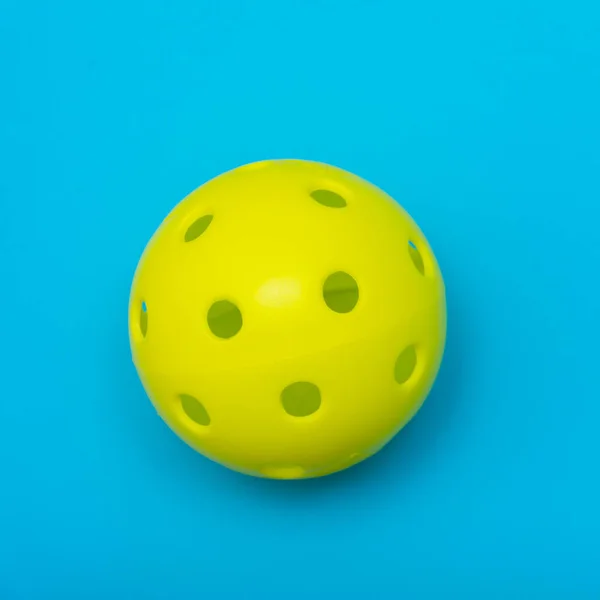 コピースペースでスポーツやアクティビティを象徴するソリッドアクアブルーのフラットレイアウトの背景に明るい黄色のピックルボールまたはホイップボール — ストック写真