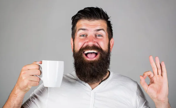 Good morning, man tea, ok. Smiling hipster man with cup of fresh coffee, Happy man showing ok sign. Morning concept. Handsome bearded man holds cup of coffee, tea. Bearded man smiling showing sign ok — Stock Photo, Image