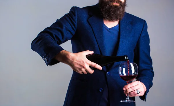 Sommelier man, degustator, winery, male winemaker. Bottle, red wine glass. Beard man, bearded, sommelier, tasting. Pouring red wine from bottle into the wineglass. Waiter pouring red wine in a glas.