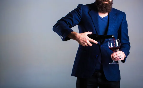 Botella, copa de vino tinto. Barbudo, barbudo, sumiller, degustación. Verter vino tinto de la botella en la copa de vino. Camarero vertiendo vino tinto en una copa. Sommelier hombre, degustador, bodega, enólogo masculino — Foto de Stock