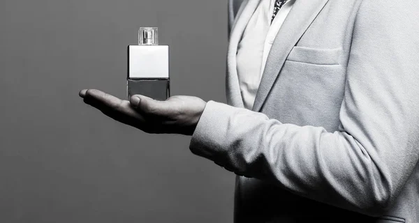 Masculine perfume, man in a suit. Man perfume, fragrance. Male holding up bottle of perfume. Perfume or cologne bottle and perfumery, cosmetics, scent cologne bottle, holding cologne. Black and white