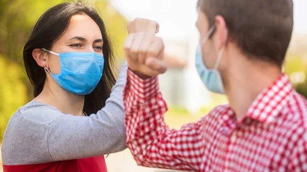 Dirsek çarpması. Yüzünde koruyucu tıbbi maske takan arkadaşları dirseklerini karantinada selamlıyorlar. Dirsek çarpması. Dirseklerle selamlaşan çift