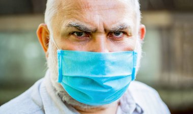 Tıbbi maske takmış yaşlı bir adamın portresi. Yaşlılar için koronavirüs tehlikesini göz önünde bulundurun. Coronavirus, hastalık, enfeksiyon, karantina, tıbbi maske. Yüz maskesi takan yaşlı bir adam. Yakın çekim.