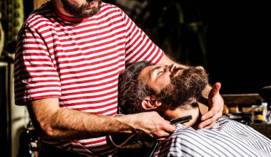 Erkekler sakallarını tıraş eder. Berber dükkanında koltukta sakallı bir erkek otururken kuaför sakalını tehlikeli bir jiletle tıraş ediyor. Berber berber dükkanında sakallı bir adamı tıraş ediyor. Yakın çekim.