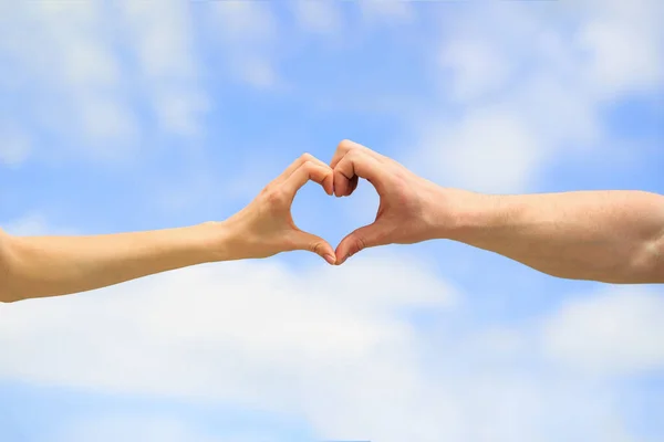 Amor, conceito de amizade. Menina e mão masculina em forma de coração amor céu azul. Feminino e homem mãos na forma de coração contra o céu. Mãos em forma de coração de amor. Coração de mãos em um fundo de céu — Fotografia de Stock