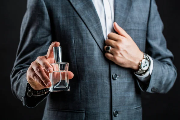 Male holding up bottle perfume. Hand in with wrist watch in a business suit. Perfume or cologne bottle and perfumery, cosmetics, scent cologne bottle, male holding cologne