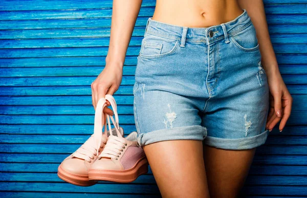 Lány egy gyönyörű alak farmernadrágban és rózsaszín cipőben. Egy lány cipőt tart a kezében. Egy nő cipőt tart. Egy nő egy pár rózsaszín cipővel a kezében. Gyönyörű derekú lány farmernadrágban. — Stock Fotó
