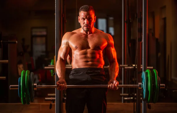 Entrenamiento muscular con barra de pesas en el gimnasio. Culturista atlético con seis manadas, abdominales perfectos, hombros, bíceps, tríceps, pecho. Entrenamiento de campanas. Tipo atlético de pie con barra, entrenamiento en el gimnasio — Foto de Stock