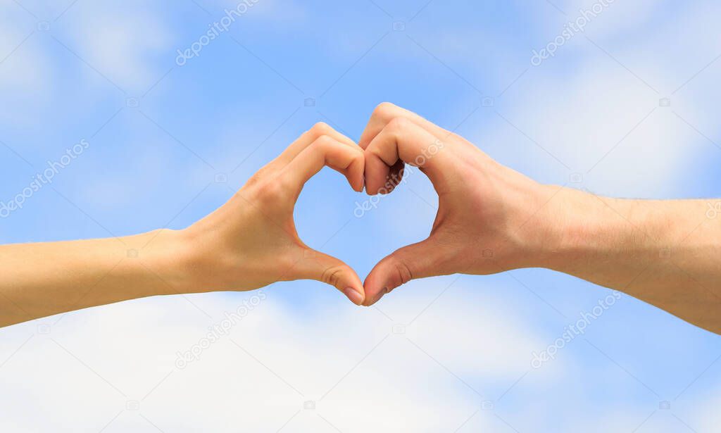 Heart from hands on a sky background. Love, friendship concept. Girl and male hand in heart form love blue sky. Female and man hands in the form of heart against the sky. Closeup