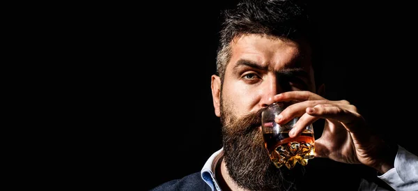 Un homme barbu tient du cognac de verre. Boire du cognac barbu. Le sommelier a le goût de boire. Un homme tenant un verre de whisky. Siroter du whisky. Portrait d'homme à la barbe épaisse. Macho buvant. Dégustation, dégustation. — Photo