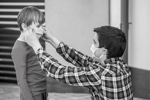 Papá con un hijo con una máscara médica. Papá le pone una máscara médica a su hijo. Coronavirus, enfermedad, infección, cuarentena, máscara médica. Blanco y negro —  Fotos de Stock